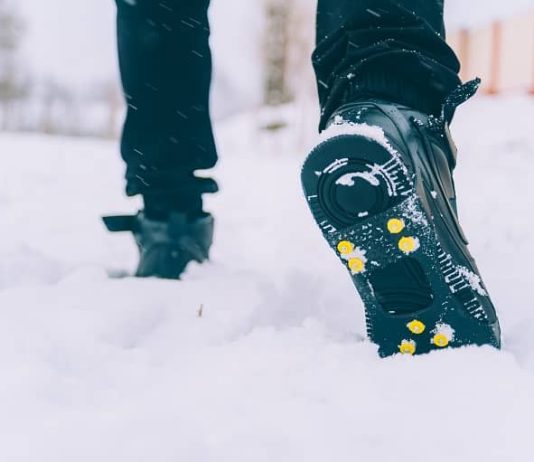 The man has ice shoes on his shoes. A people walks in the snow in winter.