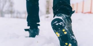 The man has ice shoes on his shoes. A people walks in the snow in winter.