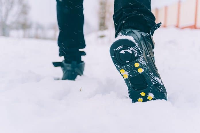 The man has ice shoes on his shoes. A people walks in the snow in winter.